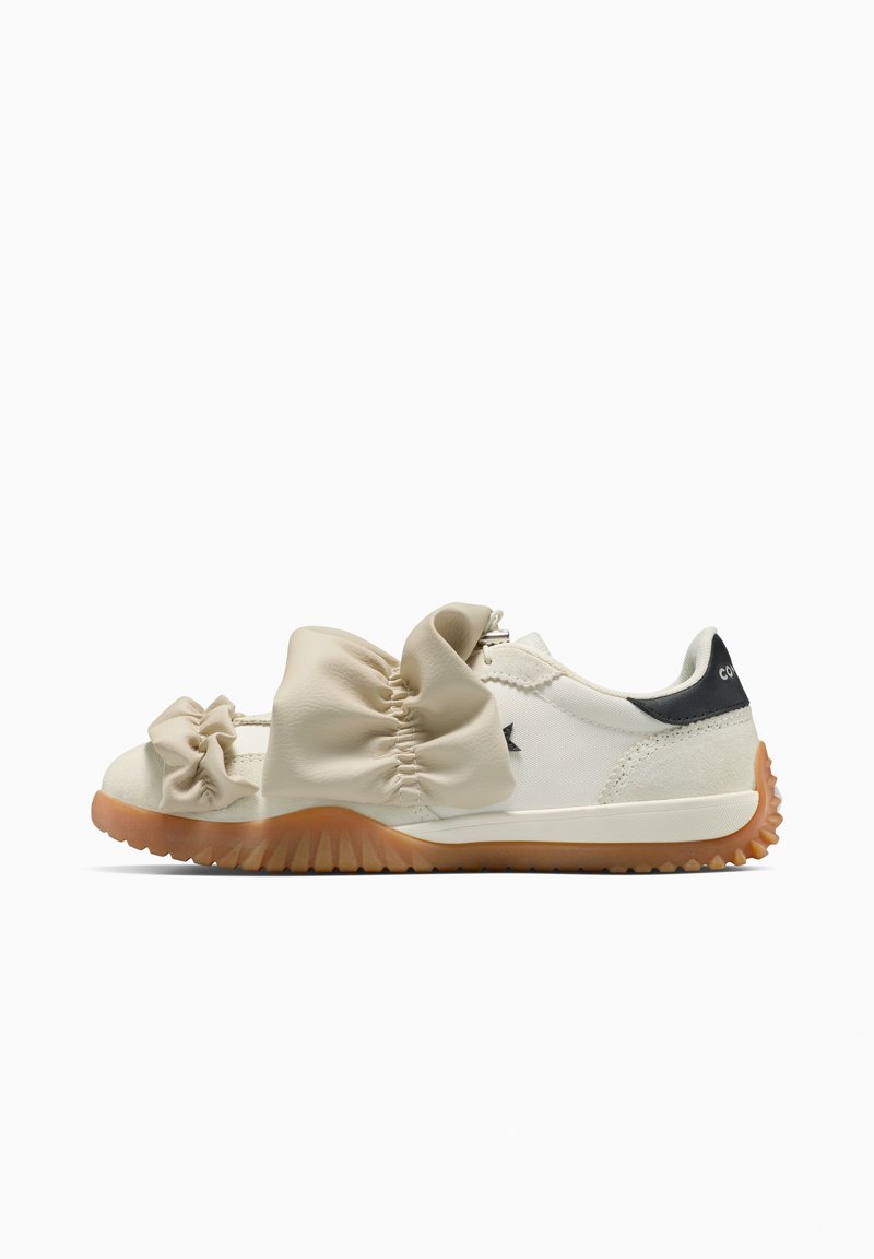 White low-top sneaker with gum sole and large gathered fabric bows across the top, viewed from the side on a white background.