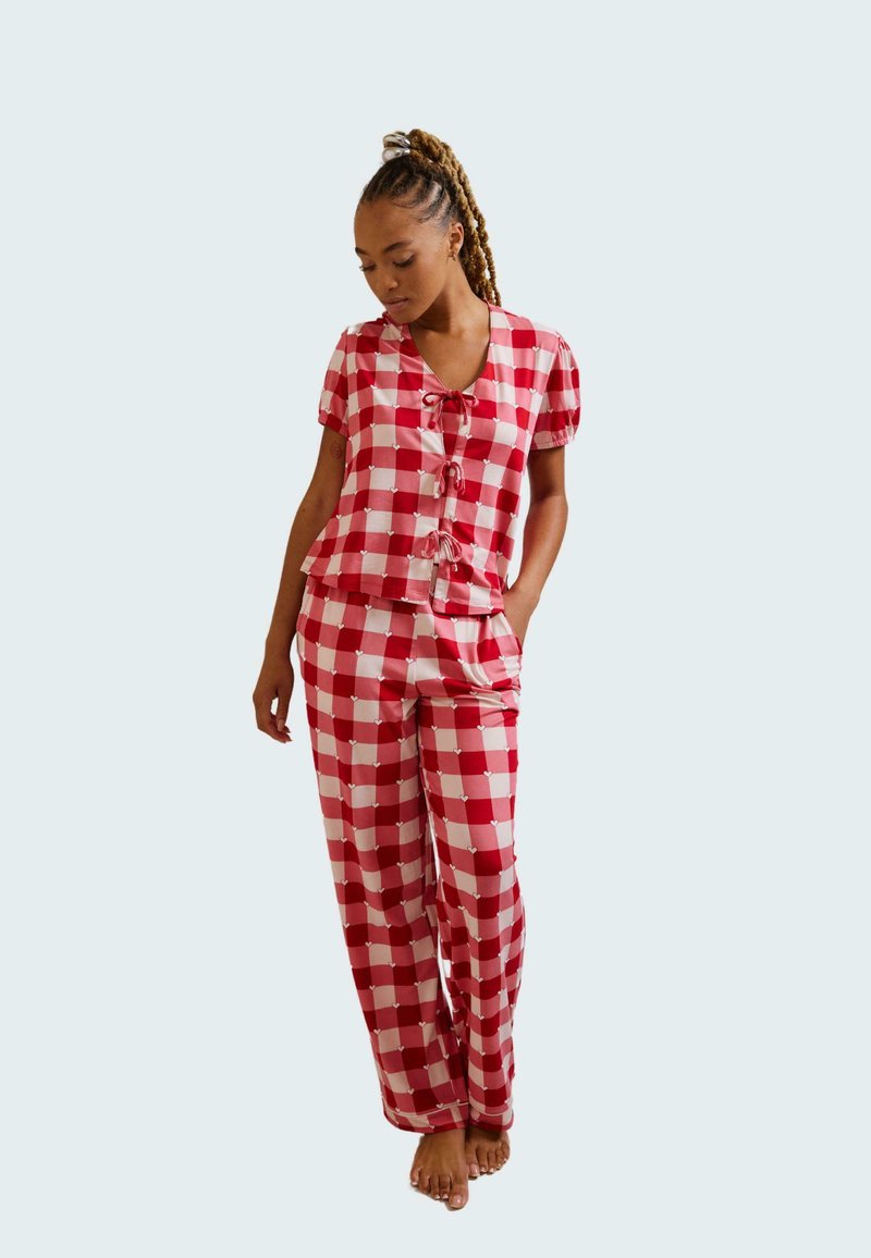 Red and white checked pajama set with short-sleeve top featuring a tie detail and matching long pants. Soft fabric with a relaxed fit.