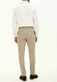 Ljust beige dressbyxor med smal passform, mjuk textur och två bakfickor, tillsammans med en vit skjorta med knappar. Bruna skor fulländar looken.