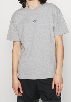 Person trägt ein graues Nike T-Shirt mit kleinem Logo auf der Brust und schwarze Nike Air Shorts.