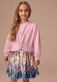 Világos rózsaszín hosszú ujjú felső csavart elülső dizájnnal és fodros ujjal; hozzáillő több színű flitteres szoknya, amely aranyból kékig átmenetes.