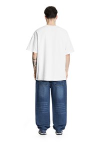 Biała bawełniana koszulka z krótkim rękawem, połączona z luźnymi niebieskimi dżinsami z widocznym przeszyciem i teksturowanym wykończeniem.