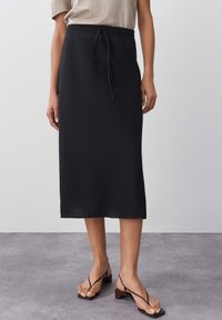 Mustat midi-hame, jossa on joustava vyötärö ja nauha. Valmistettu kevyestä kankaasta, suora siluetti. Yhdistetty litteisiin nauhakorkokengiin.