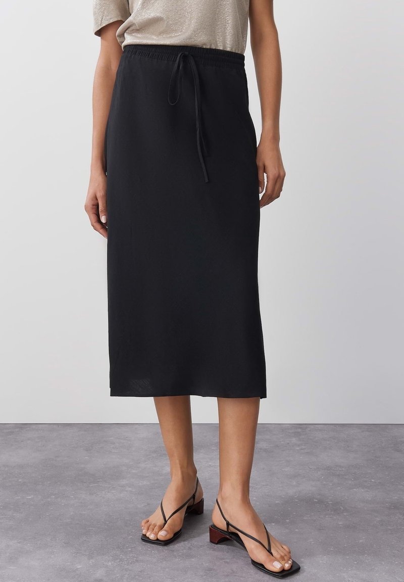 Mustat midi-hame, jossa on joustava vyötärö ja nauha. Valmistettu kevyestä kankaasta, suora siluetti. Yhdistetty litteisiin nauhakorkokengiin.