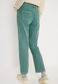Pantalones de mezclilla verdes con un corte recto, que cuentan con dos bolsillos traseros y una textura suave. Combinados con calzado de color claro.