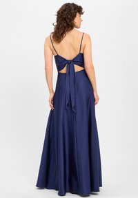 Granatowa satynowa sukienka z falującą spódnicą, odkrytymi plecami i wiązanym akcentem w talii. Posiada cienkie ramiączka i gładką fakturę.