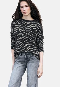 Czarny i beżowy sweter w golf z wzorem zebry o luźnym kroju, długich rękawach i fakturowanym wykończeniu, w połączeniu z jasnoszarymi jeansami z denimu.