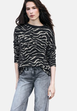 Czarny i beżowy sweter w golf z wzorem zebry o luźnym kroju, długich rękawach i fakturowanym wykończeniu, w połączeniu z jasnoszarymi jeansami z denimu.