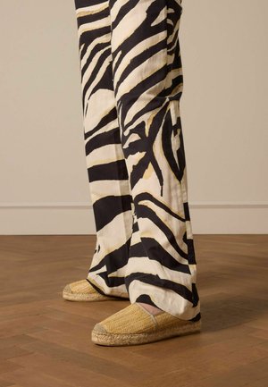 Espadrilles avec une tige en paille tissée et une semelle en caoutchouc, associées à un pantalon large à imprimé zèbre noir et blanc en tissu léger.