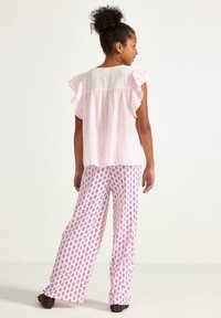 Ljusrosa, volangig topp med lös passform, kombinerad med vita byxor med ett rosa blommönster. Outfiten är lätt och avslappnad.