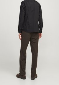 Svart långärmad skjorta med knappade ärmslut, i kombination med mörkbruna byxor. Outfiten har en avslappnad passform och rena linjer.