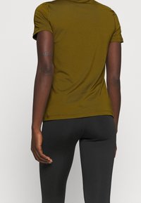Camiseta ajustada verde oliva con mangas cortas, textura suave y detalles en la costura trasera, combinada con leggings negros.