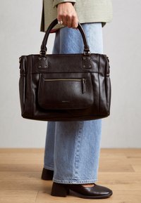 Černá kožená kabelka s dvojitými horními držadly, zipovou kapsou na přední straně, kováním v zlaté barvě a strukturovaným designem. Nošená s světle modrými džínami.