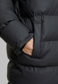 Mustat puffatakki, jossa on tasku, teksturoitu kangas ja löysä, eristetty muotoilu, jossa on kapeneva siluetti.