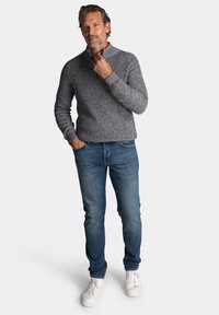Grijze gebreide trui met een halve ritssluiting, gecombineerd met blauwe jeans en witte sneakers. Casual outfit met een gestructureerde stof.