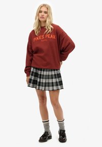 Sudadera color burdeos con el texto "PIKES PEAK", usada sobre una falda con pliegues de cuadros en blanco y negro. Combinada con calcetines grises y zapatos negros.