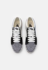 Schwarz-weiße Karomuster-Canvas-Sneaker mit weißen Schnürsenkeln, Wildlederakzenten und einem Markenetikett auf der Zunge. Klassisches Low-Top-Design.