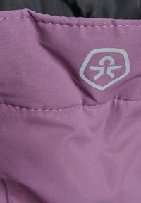 Rosa tyg med en strukturerad yta, med en grå logotyp som har en stiliserad figur inuti en sköld, och synlig sömnad längs kanten.