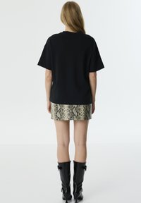 Camiseta negra de gran tamaño, combinada con una mini falda de estampado de serpiente metálico y botas negras de charol hasta la rodilla.