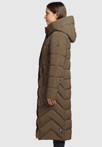 Garšs, olīvzaļš pūkains mētelis ar kapuci, ar ševronu rakstu, ar rāvējslēdzēju kabatām un logotipa uzšuvumu uz apakšmales.