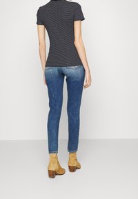 Černobílé pruhované tričko s krátkými rukávy, modré úzké džíny a béžové semišové kotníkové boty na blokovém podpatku, pohled zezadu.