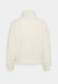 Giacca in pile di colore crema, morbida e soffice, con colletto alto e polsini a costine. Senza chiusure visibili; texture morbida e design corto.