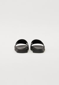 Sandales noires avec une semelle plate, un design ouvert et des doubles sangles. Surface texturée avec un minimum de matériel et des découpes sur les côtés.