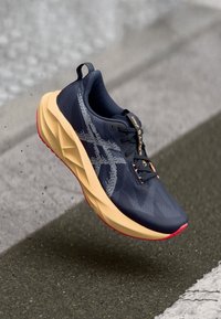 Chaussure de course de couleur marine avec une tige texturée, une semelle intermédiaire beige clair et une semelle extérieure rouge ; présente un logo sur le côté et une languette à l'arrière.
