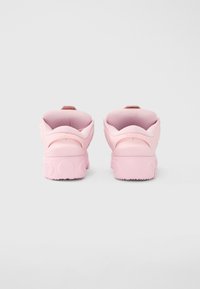 Ροζ αθλητικά παπούτσια με υφή σχεδίασης και μαξιλαρωμένη φτέρνα. Εξωτερική σόλα από καουτσούκ με κυκλικά σχέδια και μικρό λουρί στο πίσω μέρος για εύκολη χρήση.