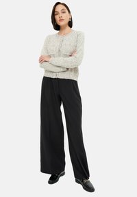 Jasnoszary sweter dzianinowy z dwoma kieszeniami, zapinany na guziki z przodu, w zestawieniu z szerokimi czarnymi spodniami i czarnymi mokasynami. Gładka faktura.