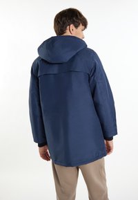 Marinblå jacka med huva, med en lös passform och sidofickor. Materialet verkar slätt med en matt yta.