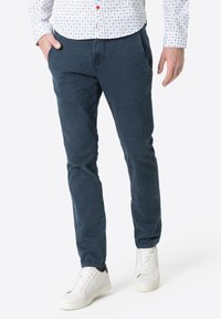 Dark blue cotton pants with a slim fit, featuring side pockets and a smooth texture. Paired with white sneakers for contrast.
