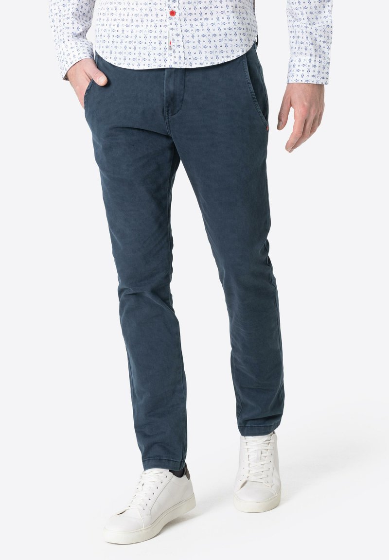 Dark blue cotton pants with a slim fit, featuring side pockets and a smooth texture. Paired with white sneakers for contrast.
