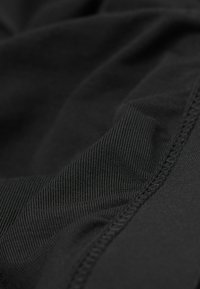 Svart tyg med en slät textur och fin ribbning. Har strukturerade sömmar och varierande ytmönster som framhäver materialets stretch.