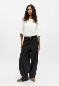 Pantalones anchos negros con cintura ajustable, combinados con una camiseta blanca de corte holgado. Tejido suave y diseño informal.