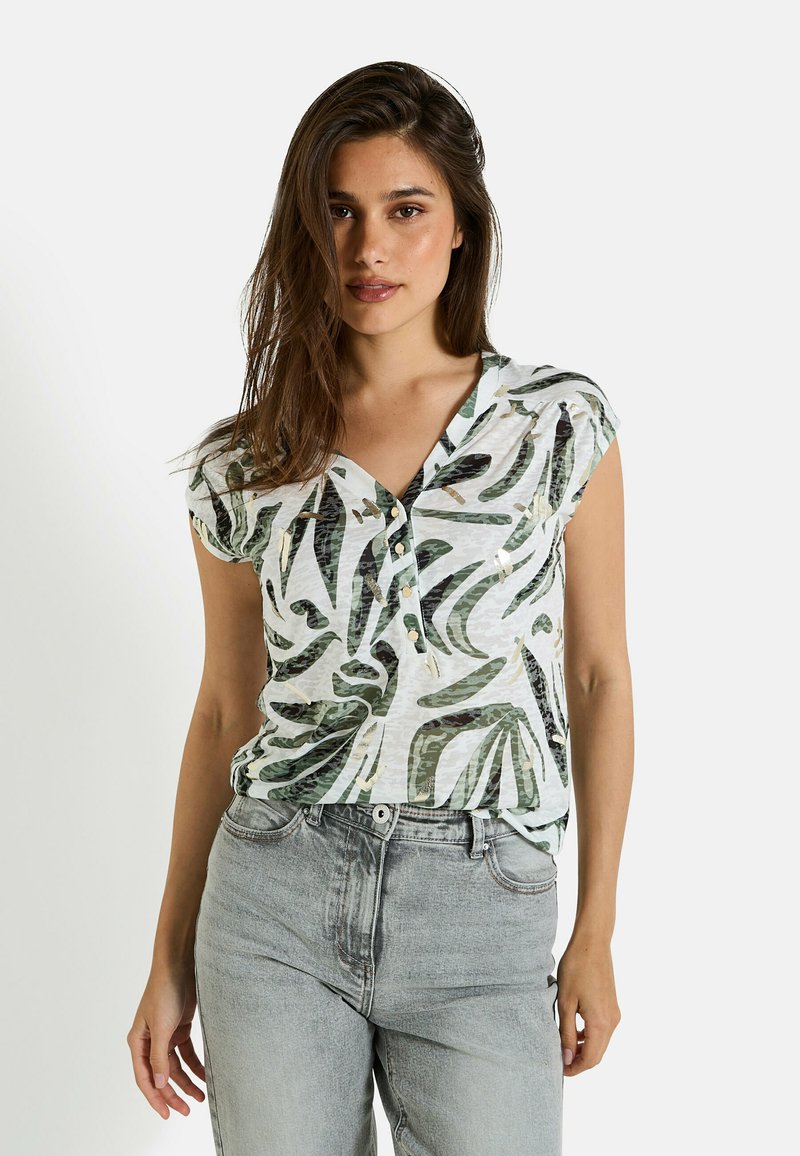 Blusa de manga corta, ligera, en blanco con patrones de hojas verdes, con escote en V y detalles de botones, acompañada de jeans de mezclilla gris.