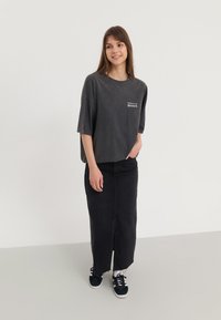 Dark grey oversized T-shirt with "Proud of the Moon" print, paired with a long black denim skirt, worn with black sneakers.