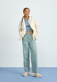Veste beige clair, crop top bleu et pantalon palazzo rayé teal. Baskets beiges chunky avec des détails tissés. Design simple et moderne.