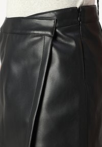 Falda de cuero negra con una textura suave, que presenta una cinturilla plana, cremallera lateral y detalle de plisado para añadir dimensión.