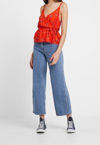 Rode bloemen peplum top met verstelbare bandjes, gecombineerd met wijde blauwe denimjeans en marineblauwe high-top sneakers. Eenvoudige en casual outfit.