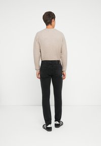 Suéter de punto color beige claro con cuello redondo, combinado con jeans de mezclilla negros. Corte ajustado con bolsillos traseros y costuras en contraste. Calzado negro.
