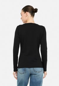 Must have mustahki pikkade varrukatega särk, mis on valmistatud pehmest kangast, ümmarguse kaelusega ja kitsas sobivuses, koos helesiniste tuhmide teksadega.