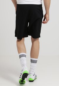 Shorts de sport noirs avec une taille élastique, associés à des chaussettes blanches à rayures noires et des crampons de football avec des accents verts.