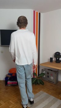 White long-sleeve shirt and light blue jeans worn by a person from behind. Black sneakers and a textured rug on a wooden floor.