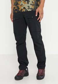 Pantalons cargo noirs en tissu léger, dotés de plusieurs poches et d'un design à jambes droites, associés à des chaussures de randonnée noires et rouges.