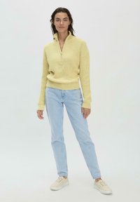 Helle gelbe, strukturierte Pullover mit einem Reißverschlusskragen, kombiniert mit hellblauen Jeans und beigen Sneakern, die einen entspannten Schnitt bieten.