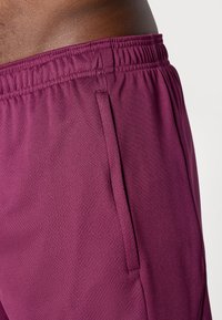 Fialové sportovní šortky s texturovaným materiálem, elastickým pasem a bočními kapsami pro pohodlí. Navrženo pro aktivní používání.