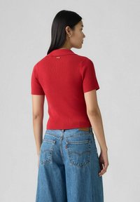 Röd ribbad kortärmad polo från med spetsig krage. Buren med ljusblå vida jeans som har bakfickor och sömnadsdetaljer.