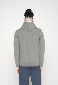 Grauer Hoodie mit einer vorderen Kängurutasche, verstellbarem Kordelzug an der Kapuze sowie gerippten Bündchen und Saum, getragen mit dunkelblauen Hosen.