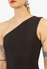 Zwarte, een-schouder jurk van ribstof met een slanke pasvorm. Beschikt over een klein zakdetail aan de zijkant en een soepele textuur.